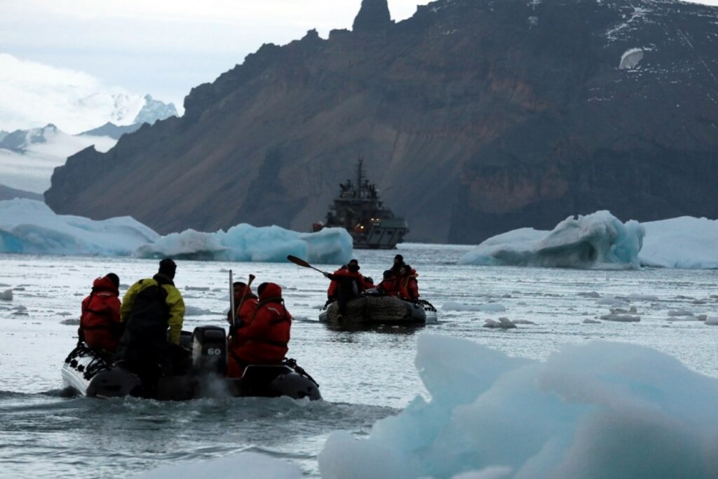 Two groups of people on zodiacs navigating through ice formations floating in the sea with land in the background