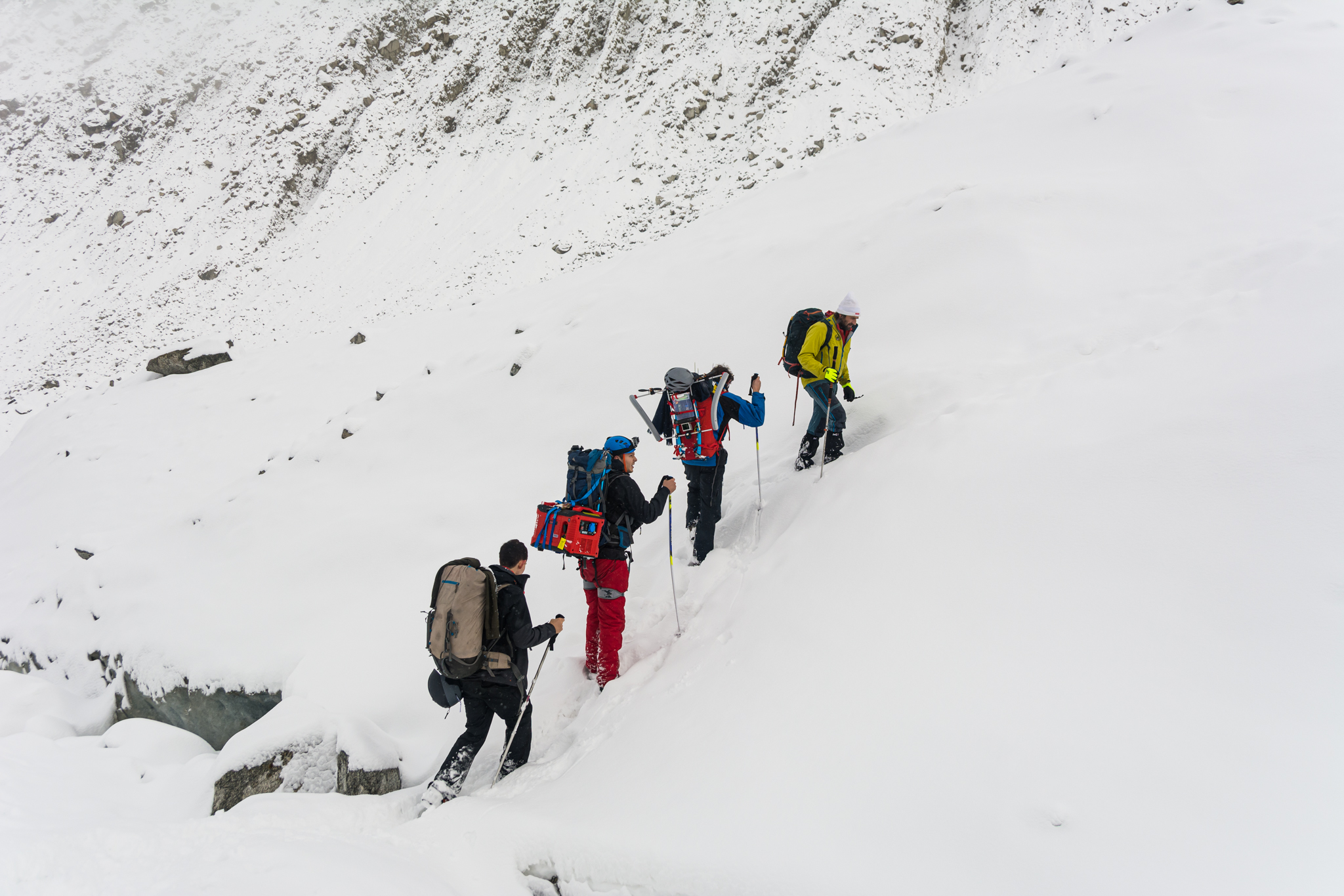 Four people with heavy backpacks climbing the snowy landscape of Mer de Glace
