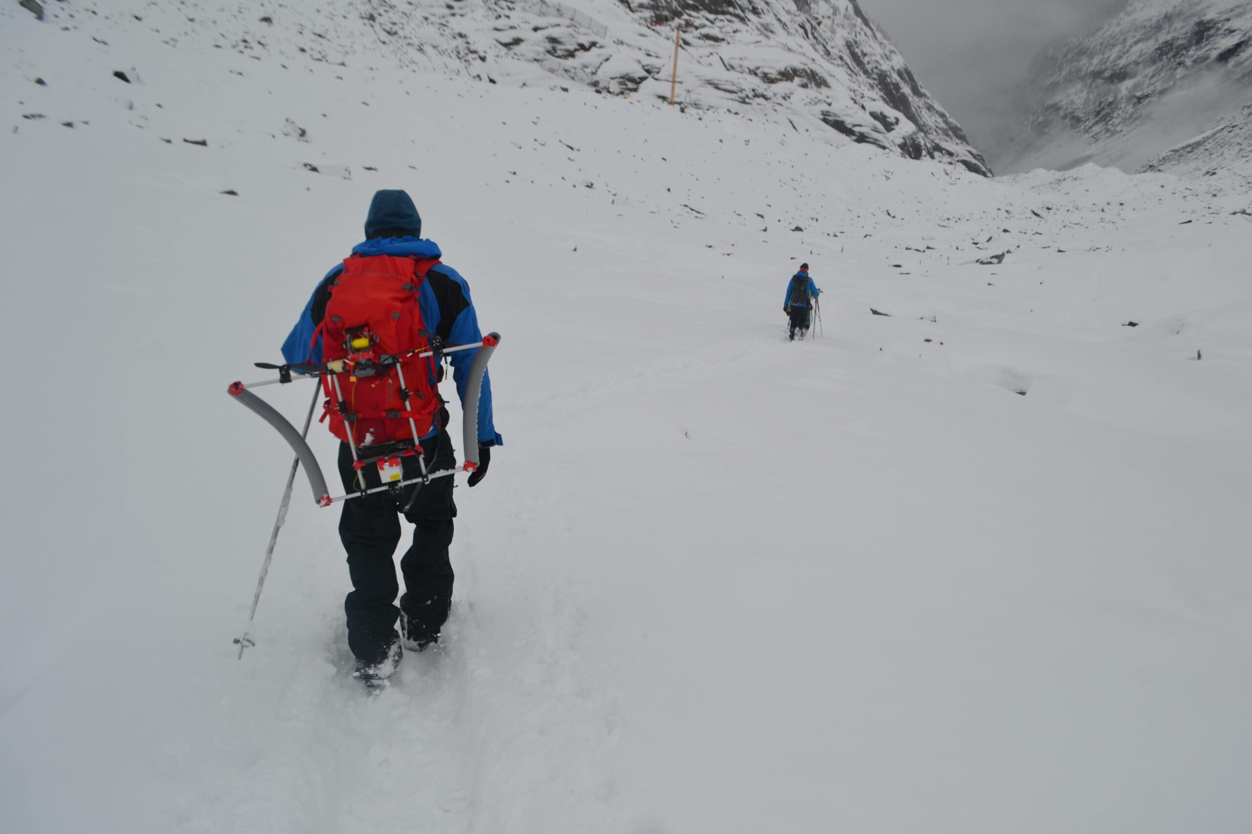 Two people descending a snowy slope carrying scientific instruments on their back